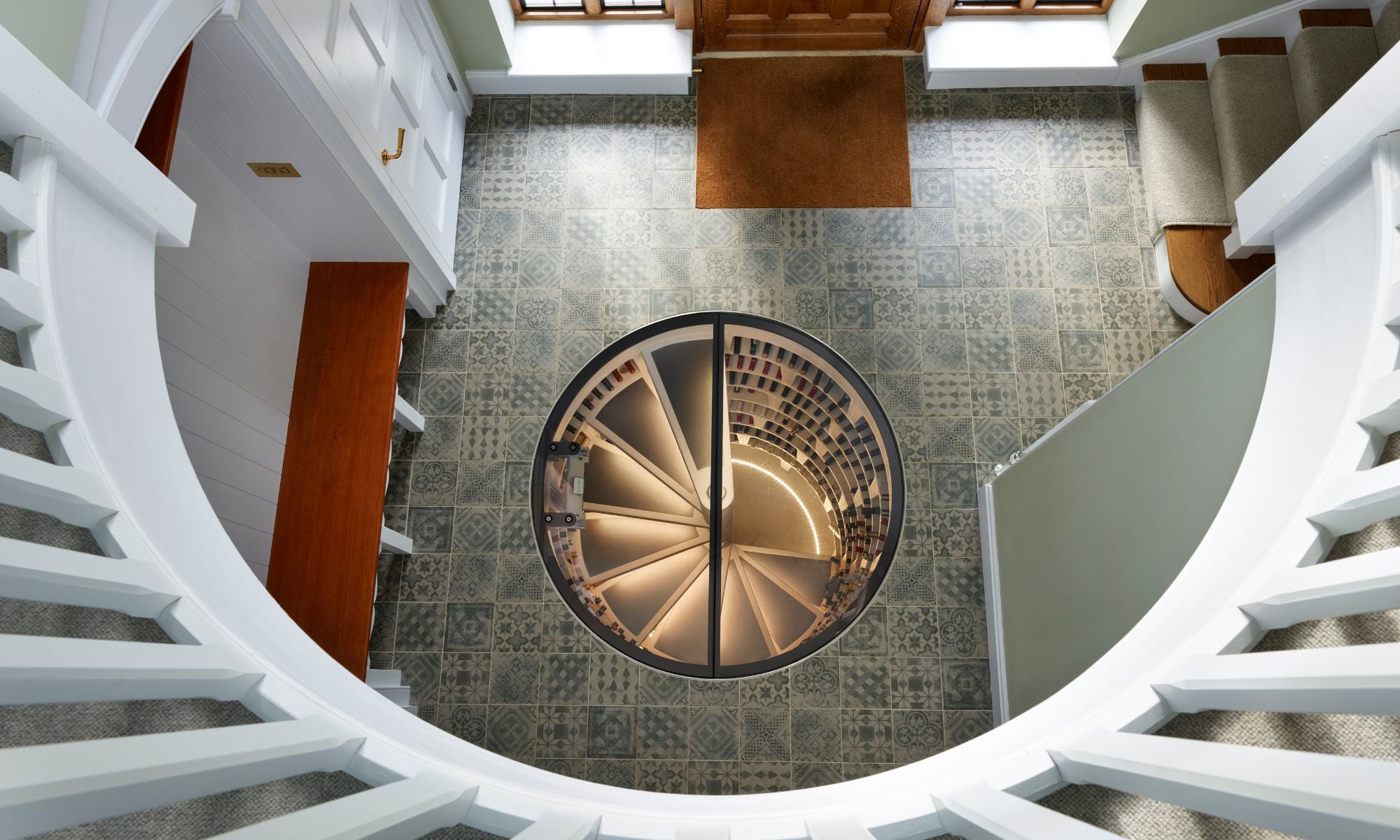 Luxury spiral wine cellar with glass door embedded in patterned tile floor, modern home entryway.