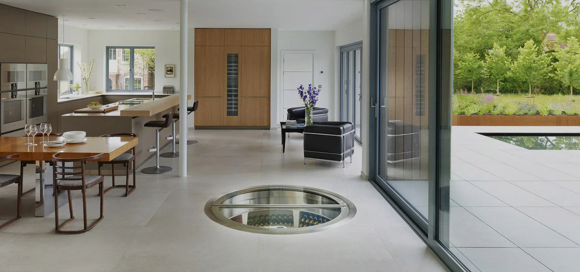 Modern kitchen and living space with a circular glass floor wine cellar and outdoor garden view