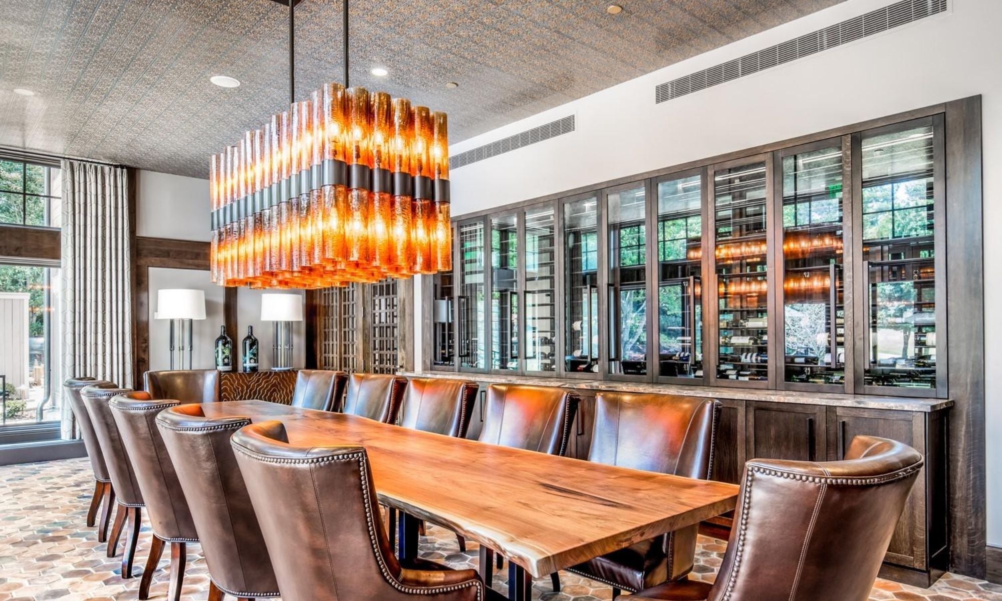 Modern wine cellar dining room with leather chairs, wood table, and glass wine storage display.