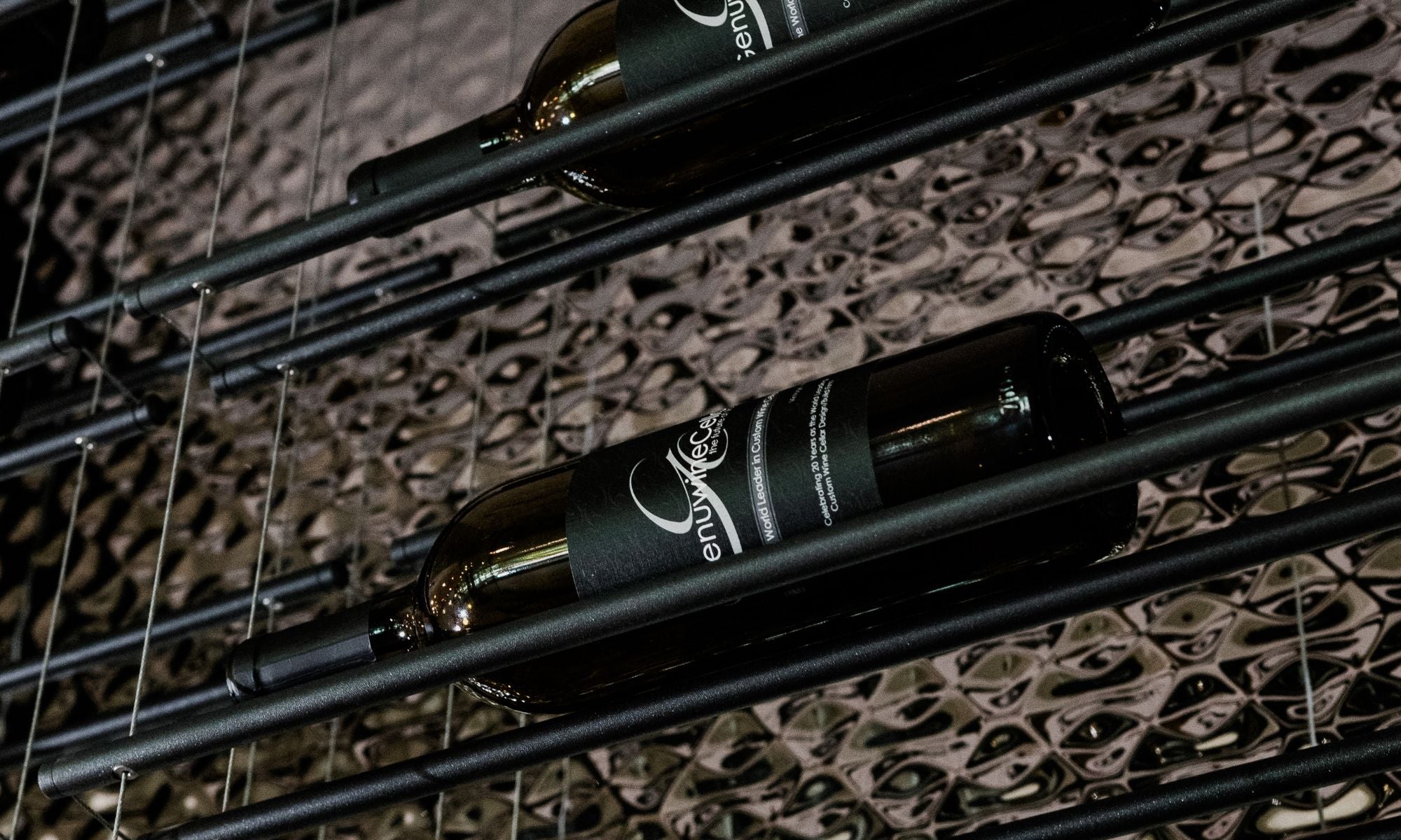Close-up of wine bottles on a modern metal wine rack with patterned wall background