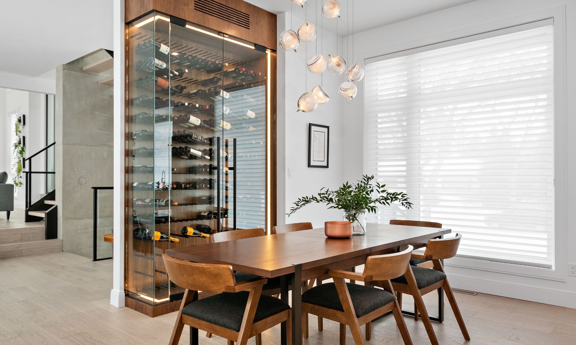 Modern dining room with a glass wine storage system, wood table, and designer lighting
