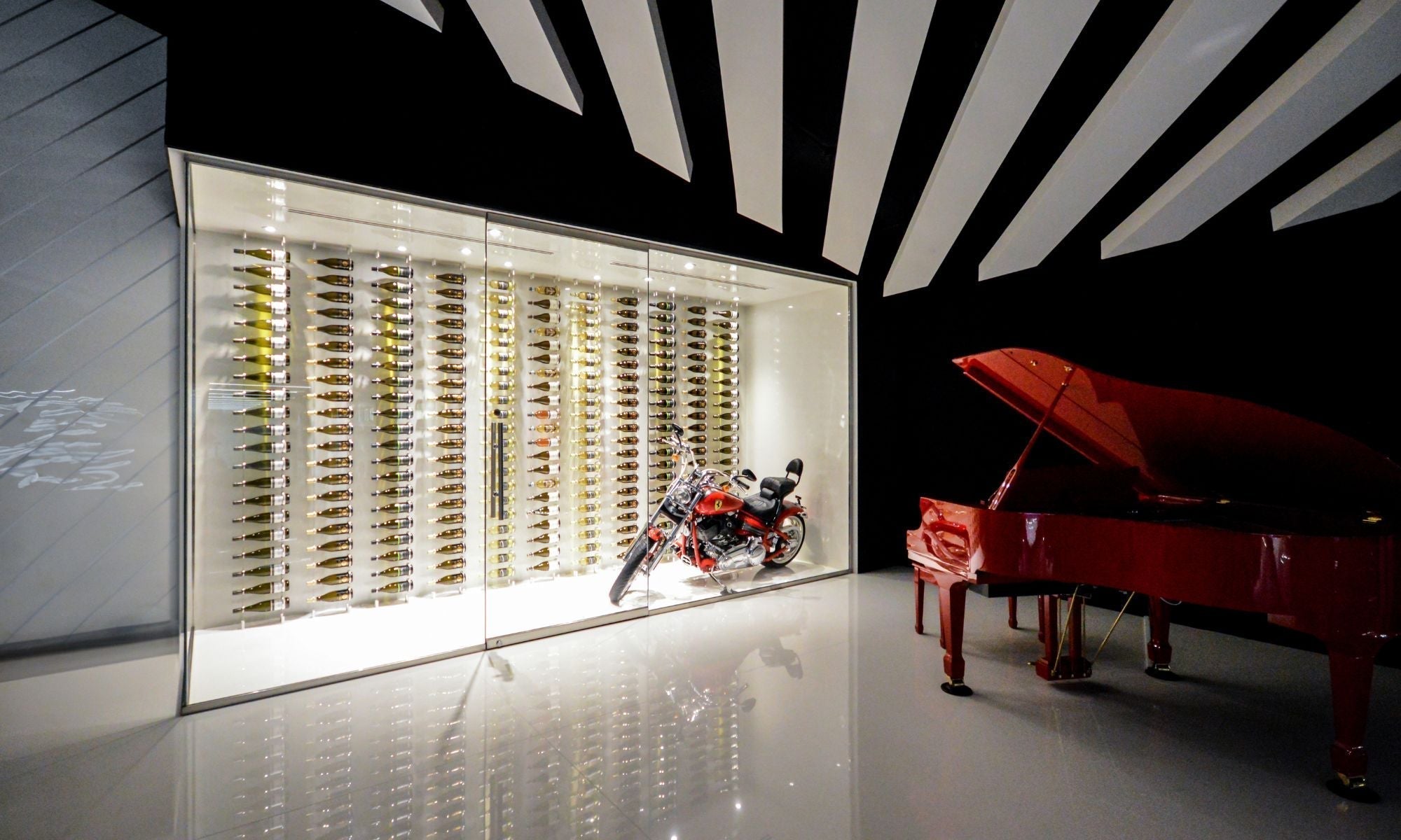 Modern glass wine wall display with mounted bottles, motorcycle, and red grand piano in luxury room