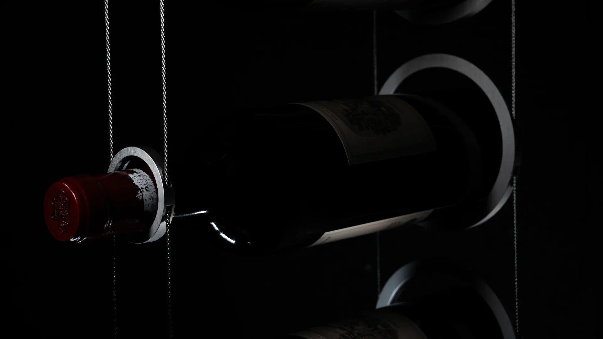 Modern cable wine rack system holding a bottle horizontally in a dark setting