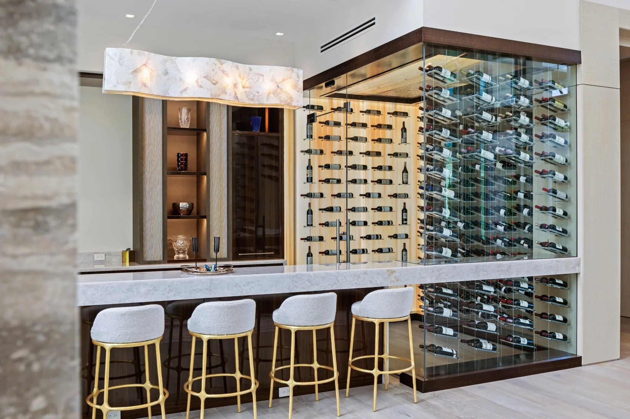 Modern glass wine cellar with luxury wine racks and elegant bar seating in a home setting