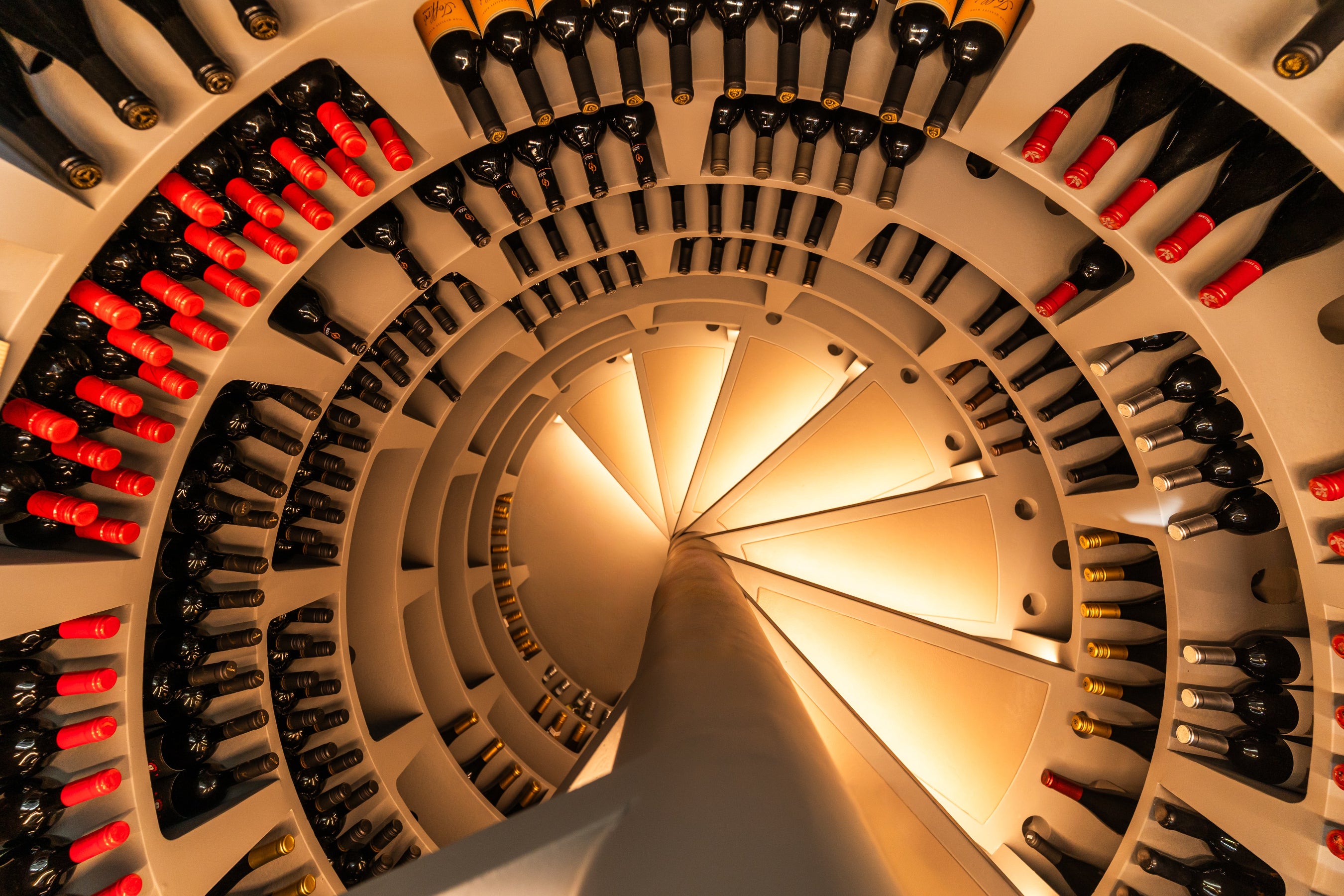 Wine bottles arranged in a spiral pattern on a white wall.